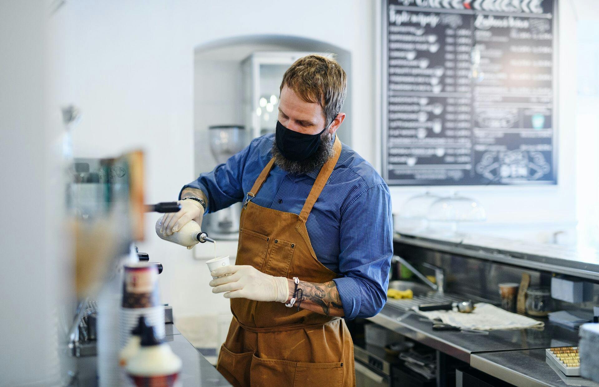 Hipster barista working with gloves, coffee shop open after lockdown quarantine.