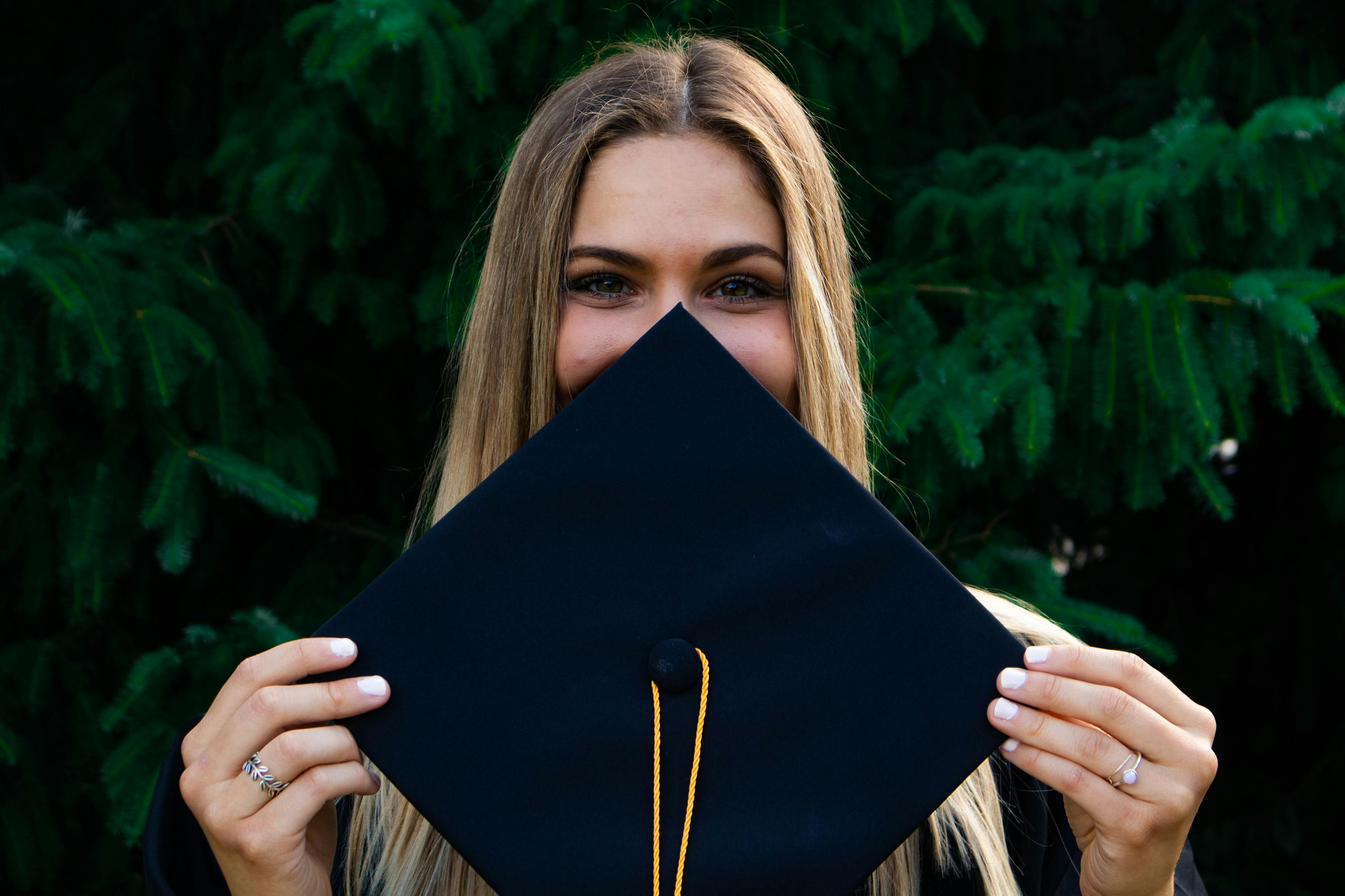 woman covering her face with graduation cap